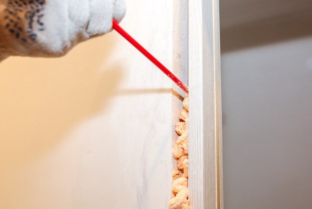 O homem está instalando a porta com uma espuma de spray. Obras de reparo. Manutenção no apartamento.