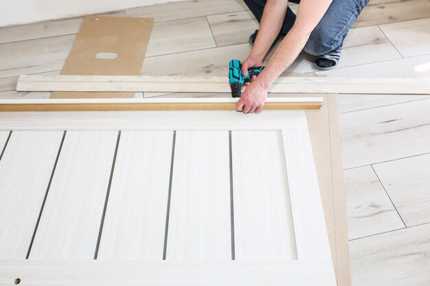 O homem está instalando as portas. Carpenter está fazendo furos com a broca nas dobradiças. Obras de reparo. Manutenção no apartamento.