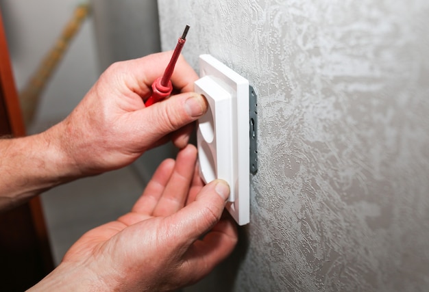 O homem está instalando o soquete. Obras de reparação de manutenção de eletricidade no apartamento. Restauração dentro de casa.