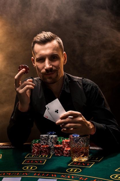 Foto o homem está jogando pôquer com um charuto e um uísque, um homem mostra duas cartas na mão, ganhando todas as fichas na mesa com fumaça espessa de cigarro. o conceito de vitória