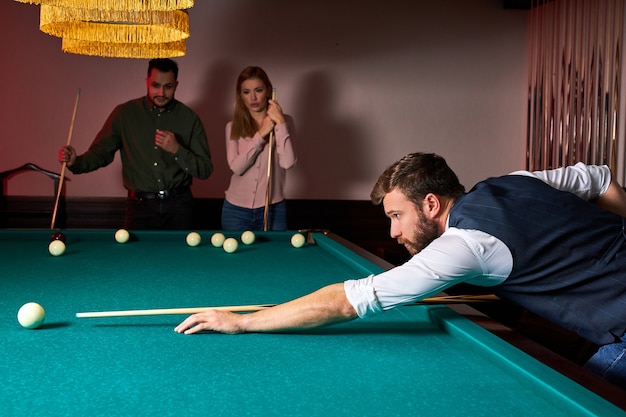 O homem está jogando sinuca, com o objetivo de lançar a bola de sinuca. cara bonito de mãos dadas na mesa de sinuca. bilhar