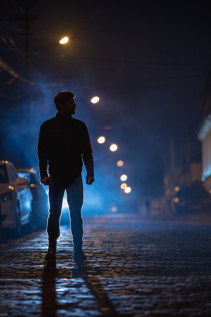 O homem está na rua enevoada. Noite à noite. Foto com lente telefoto