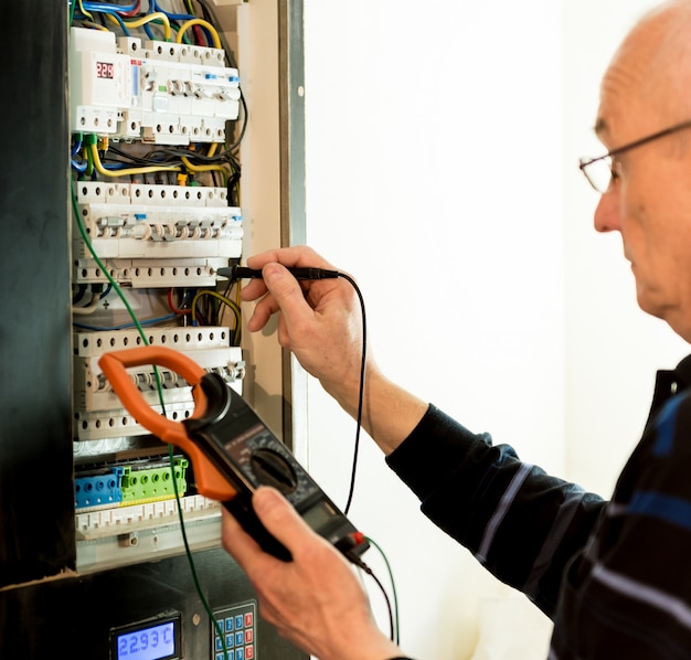 O homem está reparando a tensão do painel de distribuição com interruptores automáticos.