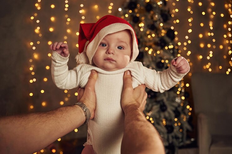 Foto o homem está segurando um bebezinho que está no chapéu de papai noel dentro de casa com guirlandas festivas de ano novo atrás