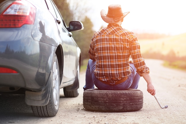 O homem está sentado na estrada perto do carro na natureza