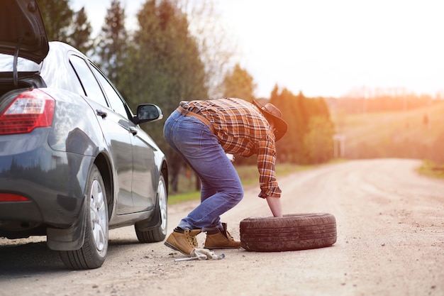 O homem está sentado na estrada perto do carro na natureza