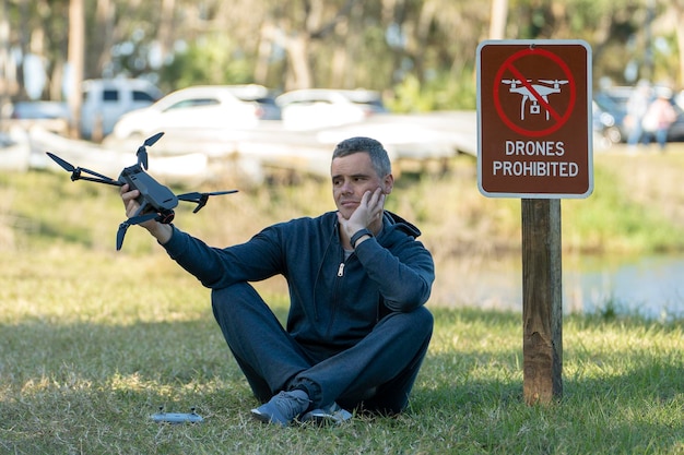 O homem está triste porque não tem permissão para voar seu quadcopter parque estadual nenhuma área de drone Operador não é autorizado a usar UAS perto de sinal de restrição