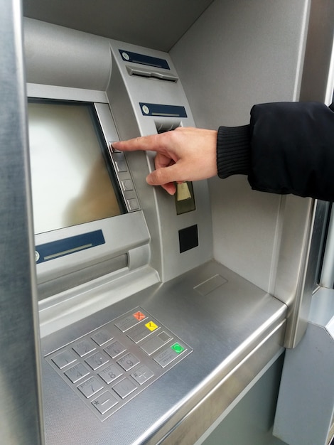 Foto o homem está usando a máquina atm com cartões de crédito e inserindo pin / código de acesso no teclado.