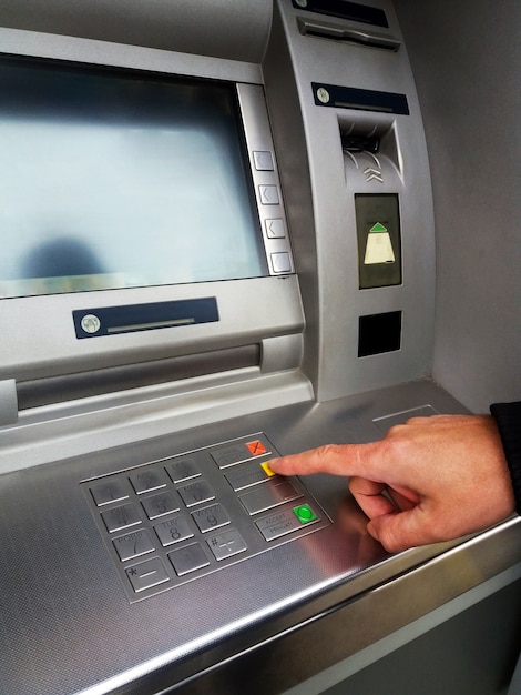 O homem está usando a máquina ATM com cartões de crédito e inserindo PIN / código de acesso no teclado.