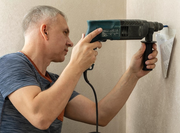 O homem faz um buraco na parede as mãos masculinas seguram uma furadeira elétrica para fazer um buraco com uma broca diy ...