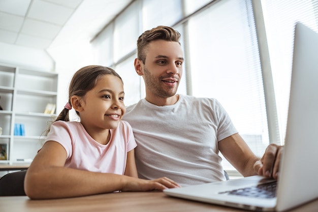 O homem feliz e uma garota com um laptop sentados na mesa