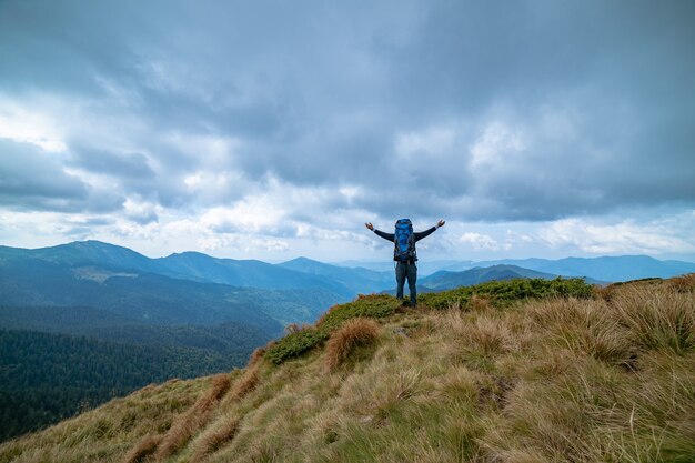 O homem feliz em pé na montanha no fundo de nuvens chuvosas