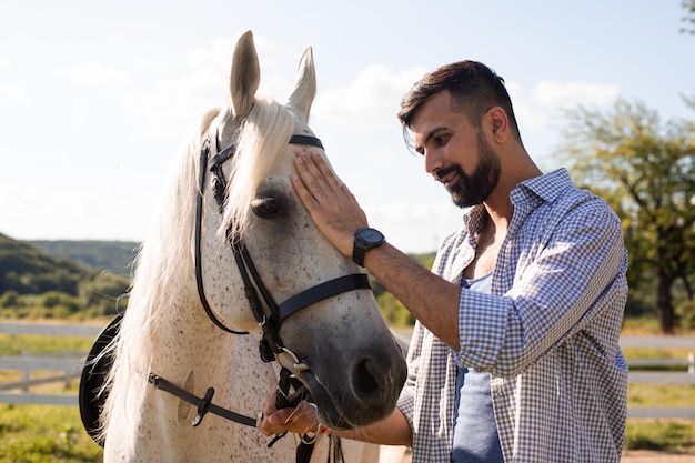 O homem feliz está acariciando um cavalo branco em um rancho