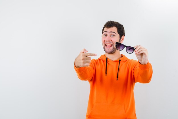 O homem feliz está mostrando seus óculos com o dedo indicador no fundo branco