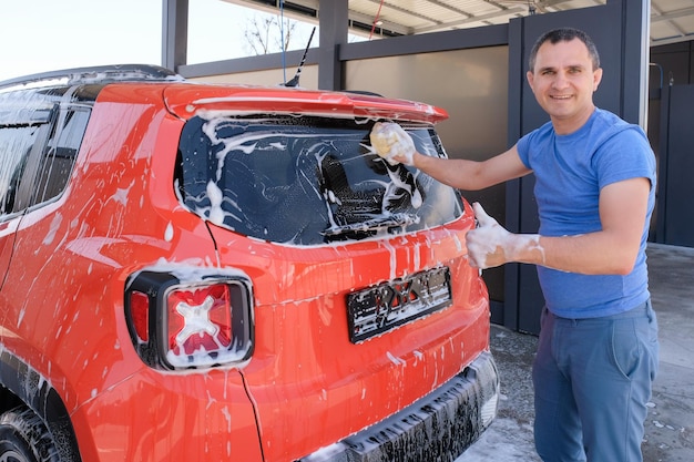 O homem feliz lava um carro em uma lavagem de carro Carro na espuma