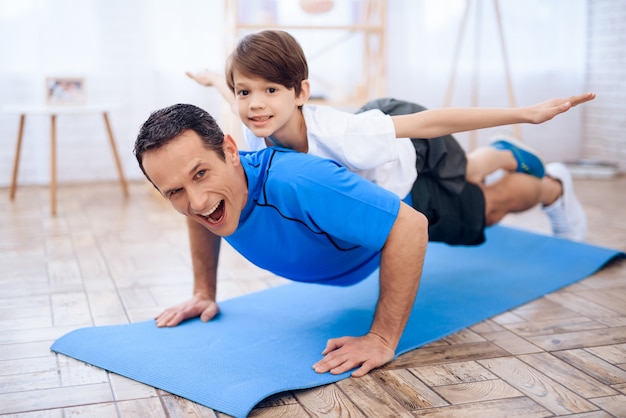 O homem flexionado do chão com o menino nas costas.