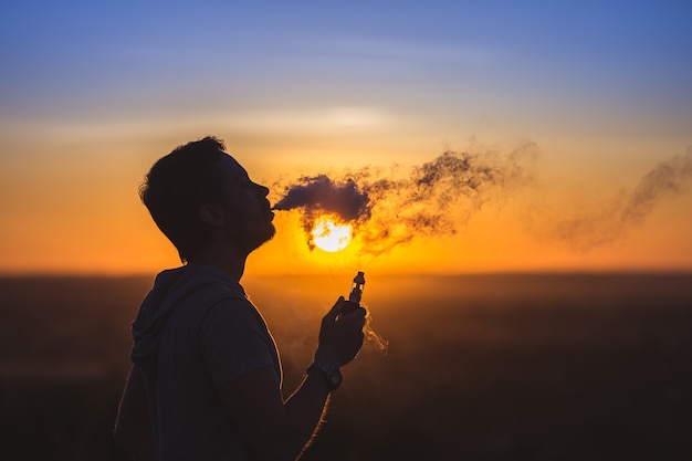 O homem fuma um cigarro eletrônico no fundo do pôr do sol