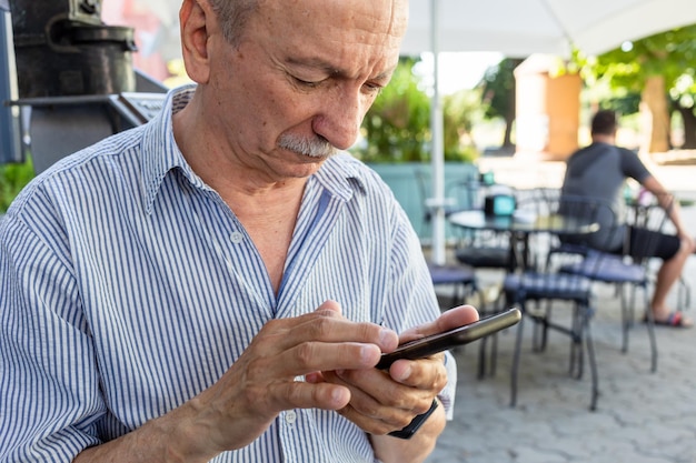 O homem idoso está segurando um telefone celular nas mãos