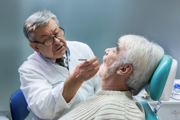 O homem idoso no estomatologista dentista está examinando a alta experiência do paciente em medicina