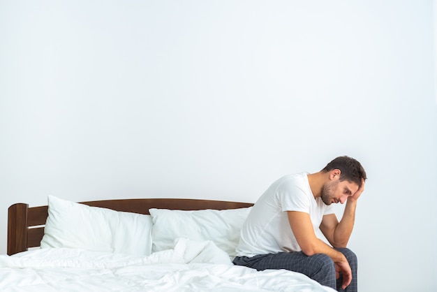 O homem infeliz sentado na cama no fundo branco