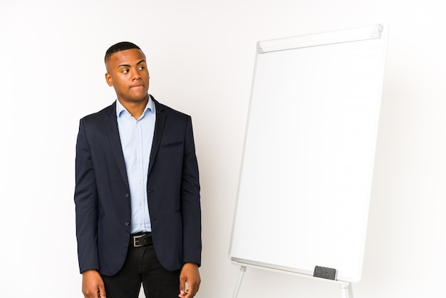 O homem latino novo com um quadro branco isolado no branco confuso, sente duvidoso e inseguro.