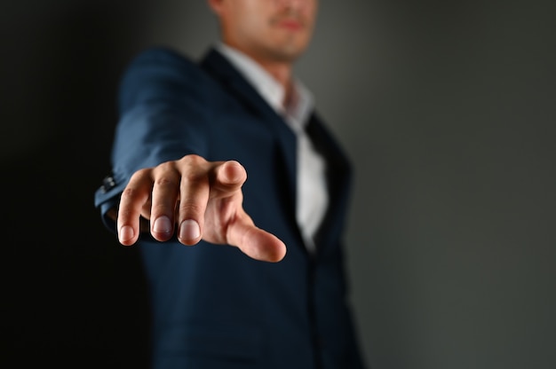 O homem mantém o dedo indicador à sua frente. Um homem de terno aponta um dedo para a frente em um espaço preto. Conceito: clique no botão, especifique especificar. Foto de alta qualidade