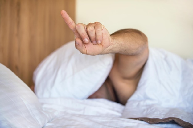 O homem na cama escondeu a cabeça debaixo do travesseiro e não quer acordar