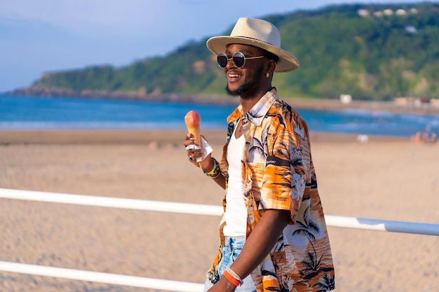 Foto o homem negro étnico aproveita as férias de verão na praia comendo sorvete