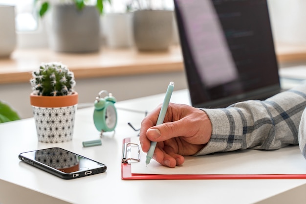 O homem no escritório trabalha em um laptop e faz anotações em um gerente de projeto ou desenvolvedor de notebook