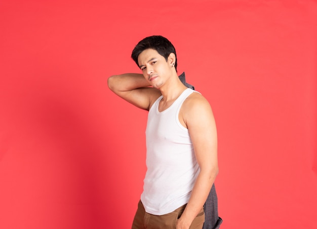 O homem novo considerável asiático com o músculo grande que veste a preensão branca da mão da veste decola a posição da camisa isolada no tiro vermelho da parede.