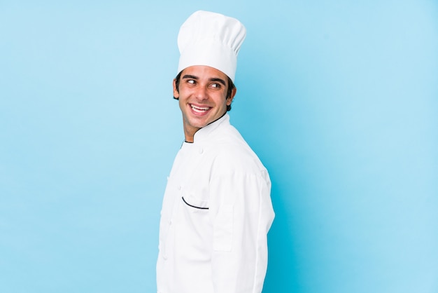 O homem novo do cozinheiro isolado olha de lado o sorriso, alegre e agradável.