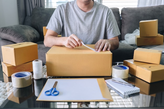 O homem novo do sme do empreendedor recebe o cliente do pedido e o trabalho com empacotamento classifica o mercado em linha da entrega da caixa