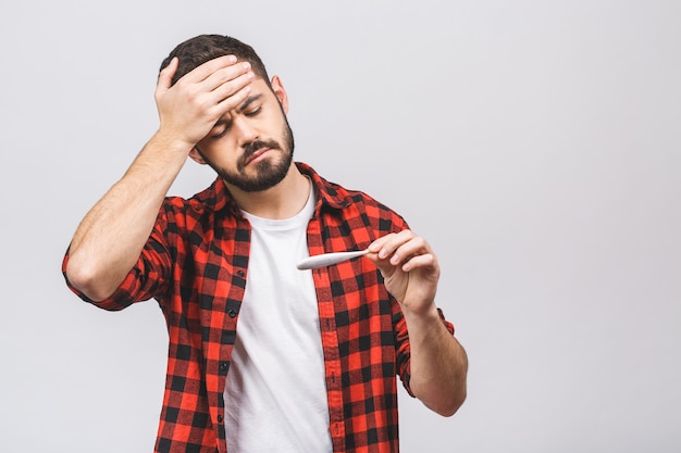 O homem novo doente olha um termômetro isolado contra o fundo branco.