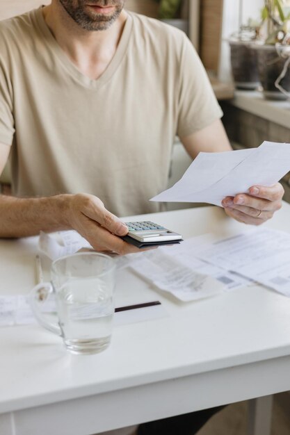 O homem paga contas e serviços públicos conta o valor das despesas e receitas na calculadora Alfabetização financeira e hipoteca ou pagamento de aluguel