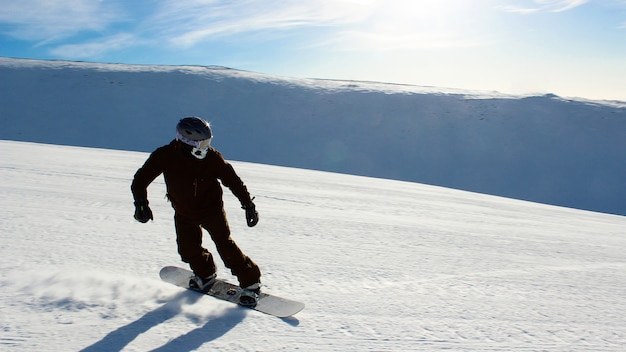 O homem praticando snowboard na encosta da montanha. entretenimento ativo de inverno em um dia frio e claro com neve