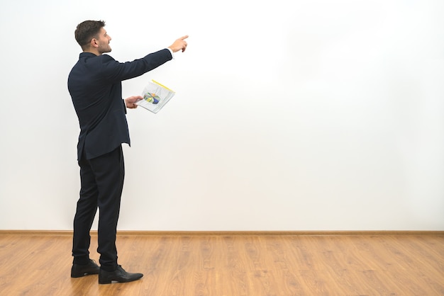 O homem segurando papéis e gesticulando no fundo da parede branca