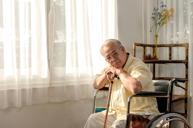 O homem sênior asiático solitário estava doente e sentado na cadeira de rodas. Estilo de vida em idade de aposentadoria e ficar em casa sozinho.