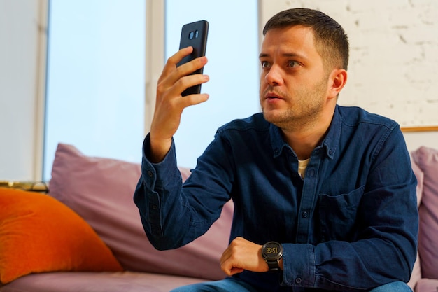 O homem senta no sofá e usa smartphone