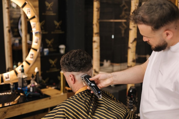 O homem sentado na barbearia durante o barbeiro cortou o cabelo atrás da visão do processo