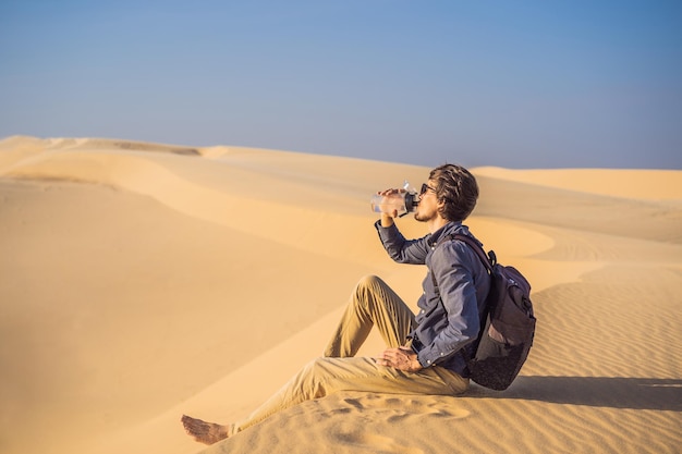 O homem sente sede e bebe água no deserto.