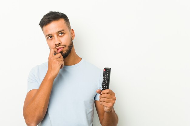 O homem sul-asiático novo que guarda um controlador da tevê relaxou o pensamento sobre algo que olha um espaço da cópia.