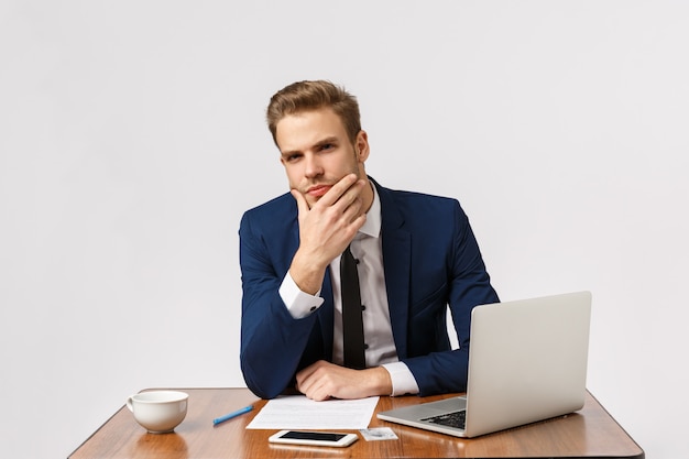 O homem tendo uma conversa séria, presumir alguma coisa, tem um pensamento profundo sobre as palavras dos colegas de trabalho. empresário bonito no escritório, sentado tocando o queixo como pensamento, fundo branco