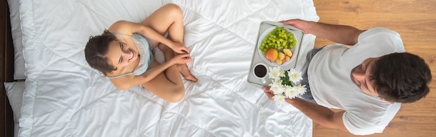 O homem trazendo um café da manhã para uma mulher na vista da cama de cima