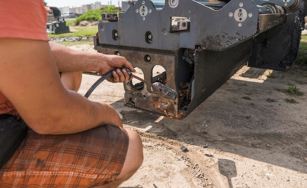 Foto o homem usa o fogo de um cilindro de gás para derreter o asfalto velho e seco na máquina de pavimentação de asfalto