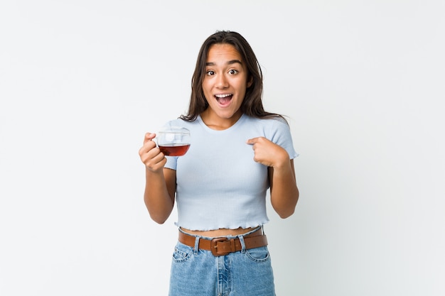 Foto o indiano novo da raça misturada que guarda uma xícara de chá surpreendeu apontar-se, sorrindo amplamente.