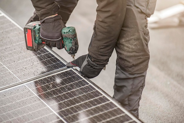 O instalador do painel solar torce os módulos juntos usando fixadores de alumínio e uma furadeira sem fio Trabalho de instalação no telhado e conceito de segurança com espaço para cópia