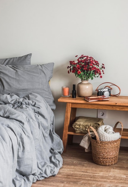 O interior do quarto uma cama com roupa de cama um buquê de crisântemos vermelhos em um banco de madeira uma cesta com xadrez uma atmosfera acolhedora e caseira