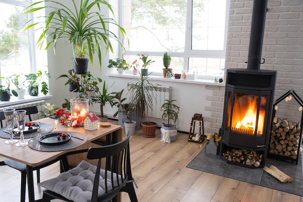 O interior festivo da casa é decorado para o Natal e o Ano Novo em estilo loft com fogão preto lareira Árvore de Natal Sala de estúdio quente com mesa posta queimando madeira aconchegante e aquecimento da casa