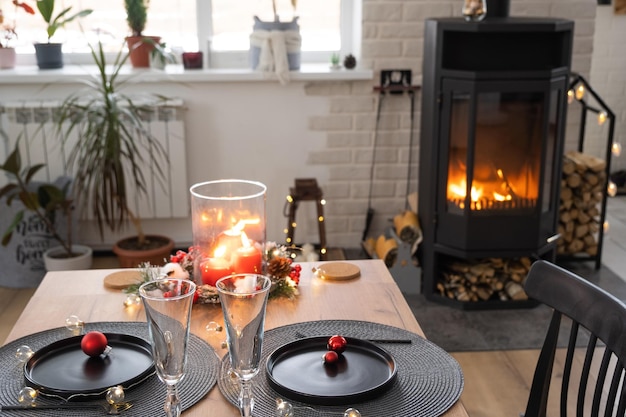 O interior festivo da casa é decorado para o Natal e o Ano Novo em estilo loft com fogão preto lareira Árvore de Natal Sala de estúdio quente com mesa posta queimando madeira aconchegante e aquecimento da casa