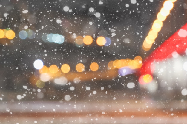 O inverno lindo desfocou o fundo da cidade à noite com neve caindo e luzes de bokeh